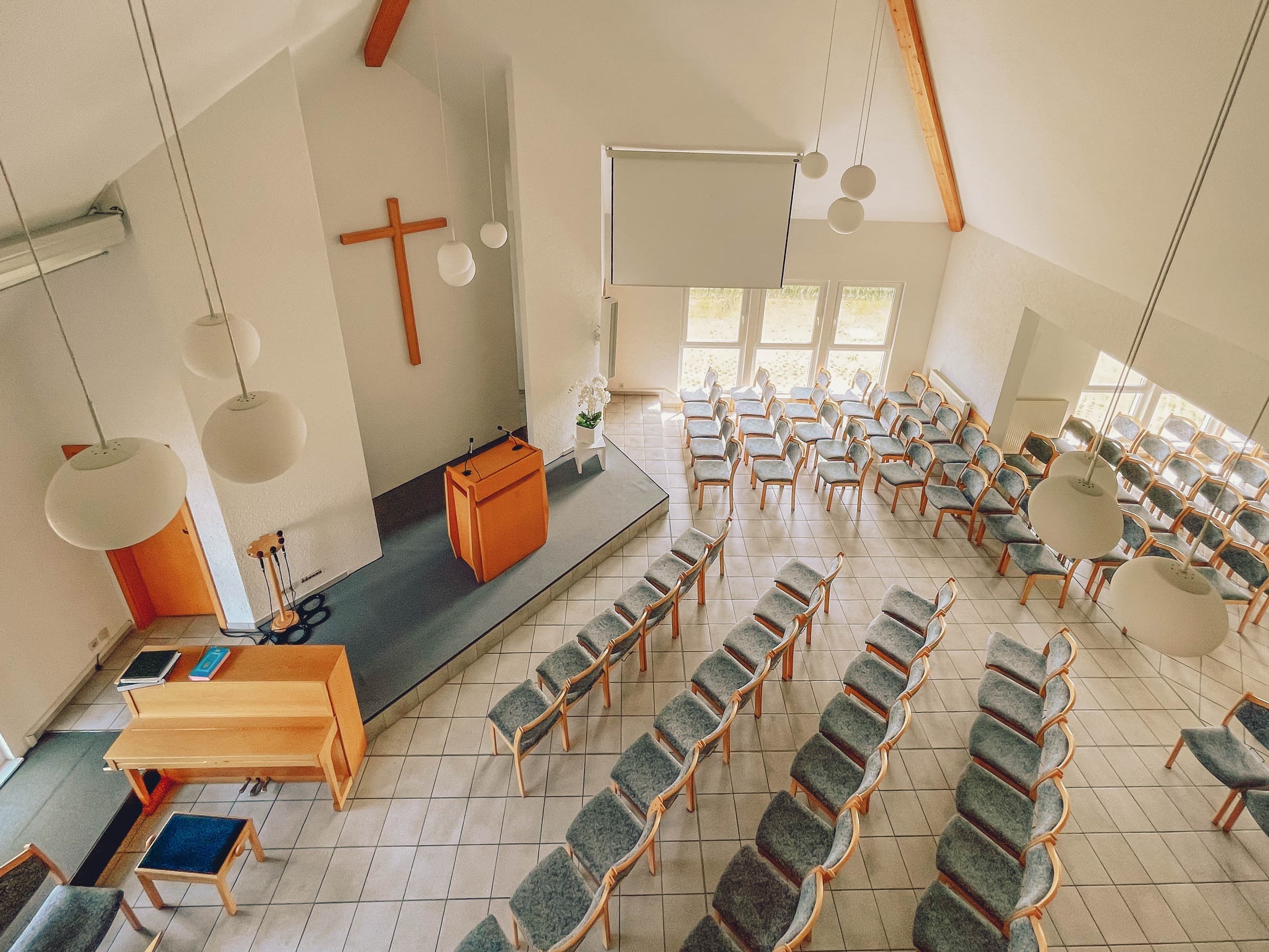 Der helle Gemeindesaal mit Holzkreuz, Rednerpult, Klavier und Stuhlreihen von oben