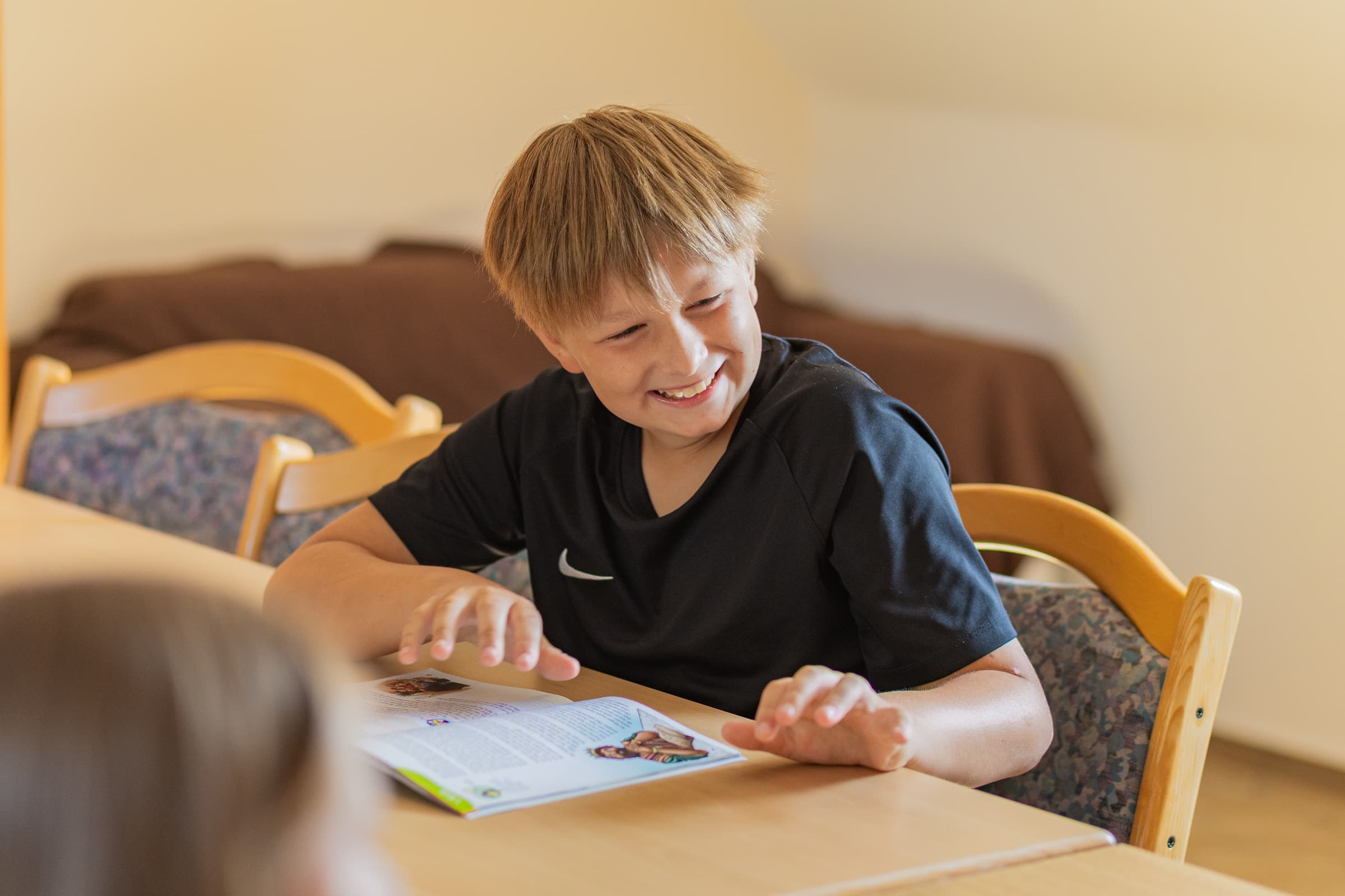 Ein Junge lacht über sein Arbeitsheft in der Kindergruppe